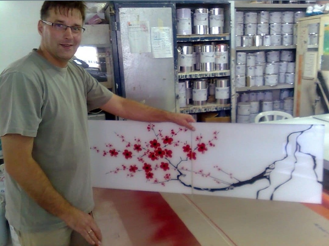 The artist presents a completed sakura glass panel in the workshop.